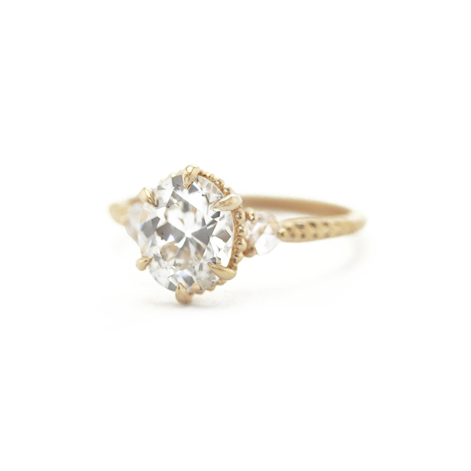 Handmade classic 3-stone engagement ring featuring large oval old mine cut diamond and rose cut diamond side stones with botanical Evergreen details in 18K yellow gold by Designer Megan Thorne