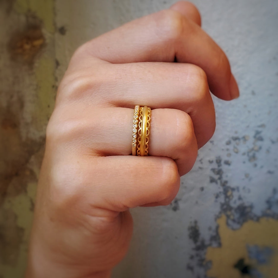 Handmade vintage inspired surprise wedding band with bezel set diamonds in 18K yellow gold by Designer Megan Thorne with other stacking rings on hand