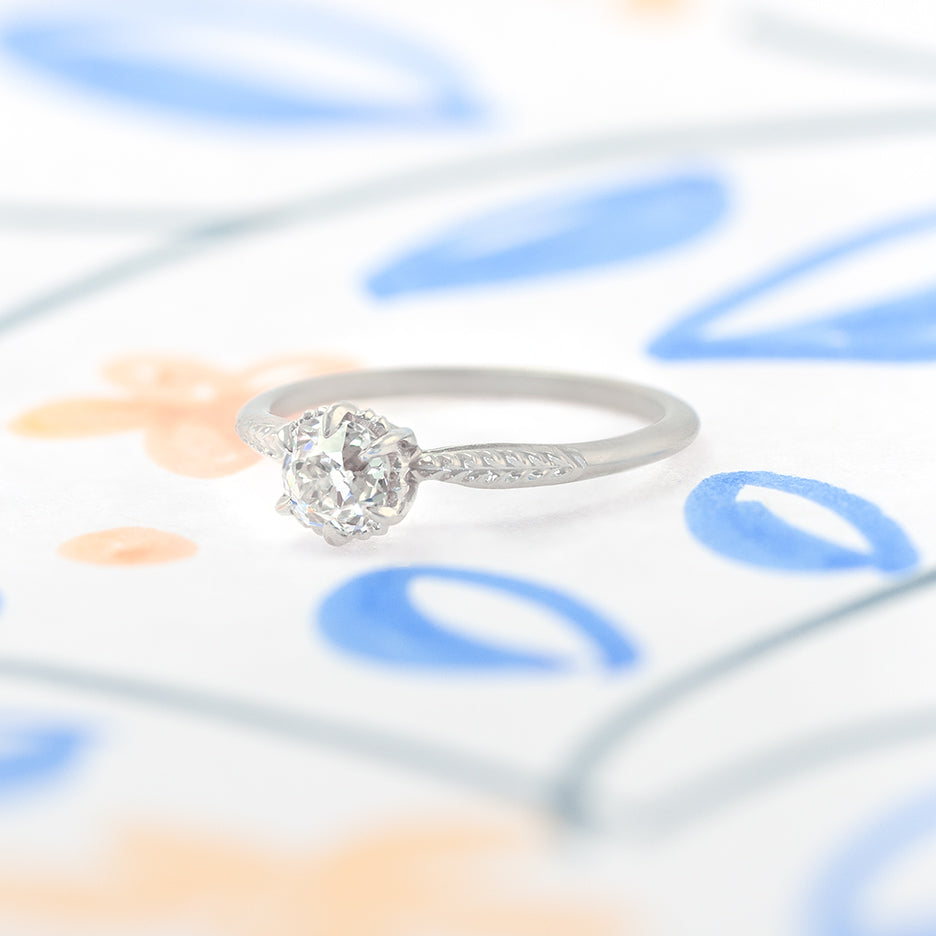 Handmade classic engagement ring featuring antique old mine cut diamond with botanical Evergreen details in 18K white gold by Designer Megan Thorne on colored background