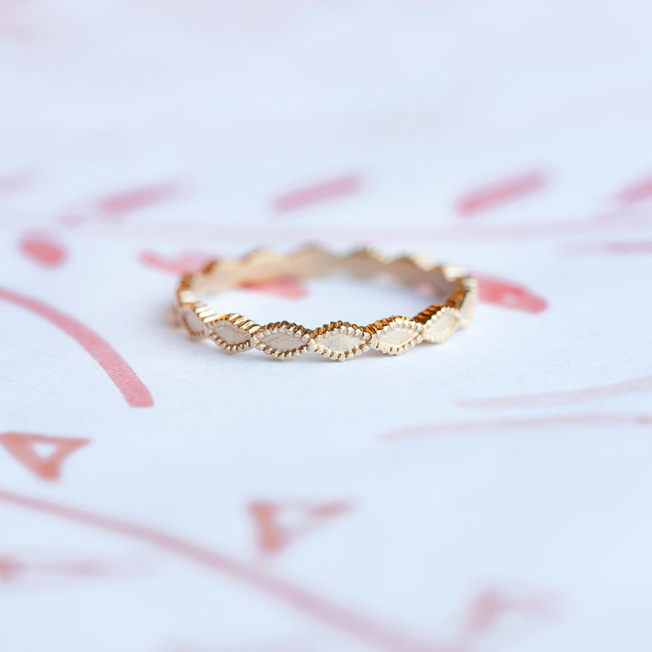 Handmade simple plain thin wedding band with triangle scalloped ribbing in 18K yellow gold by Designer Megan Thorne on colored background