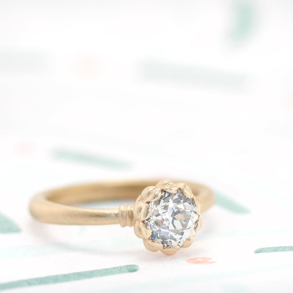 Handmade classic engagement ring with 1ct Old European Cut diamond and vintage inspired scalloped detailing with a striking symmetrical profile in 18K yellow gold by Designer Megan Thorne on colored background