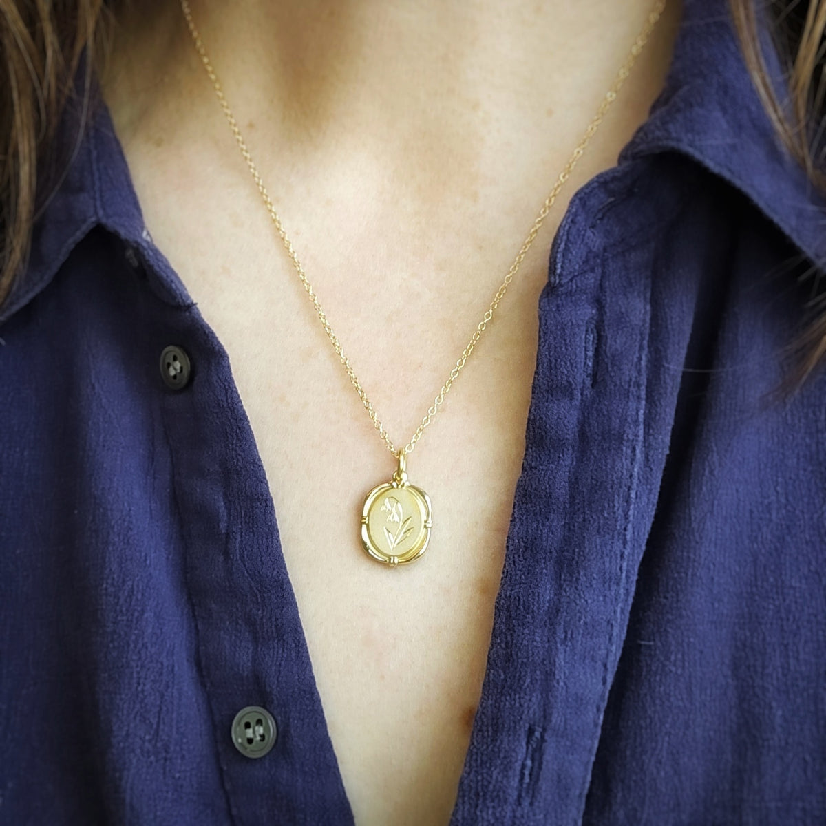 Gold necklace with a birth flower pendant worn by a person in a blue shirt.