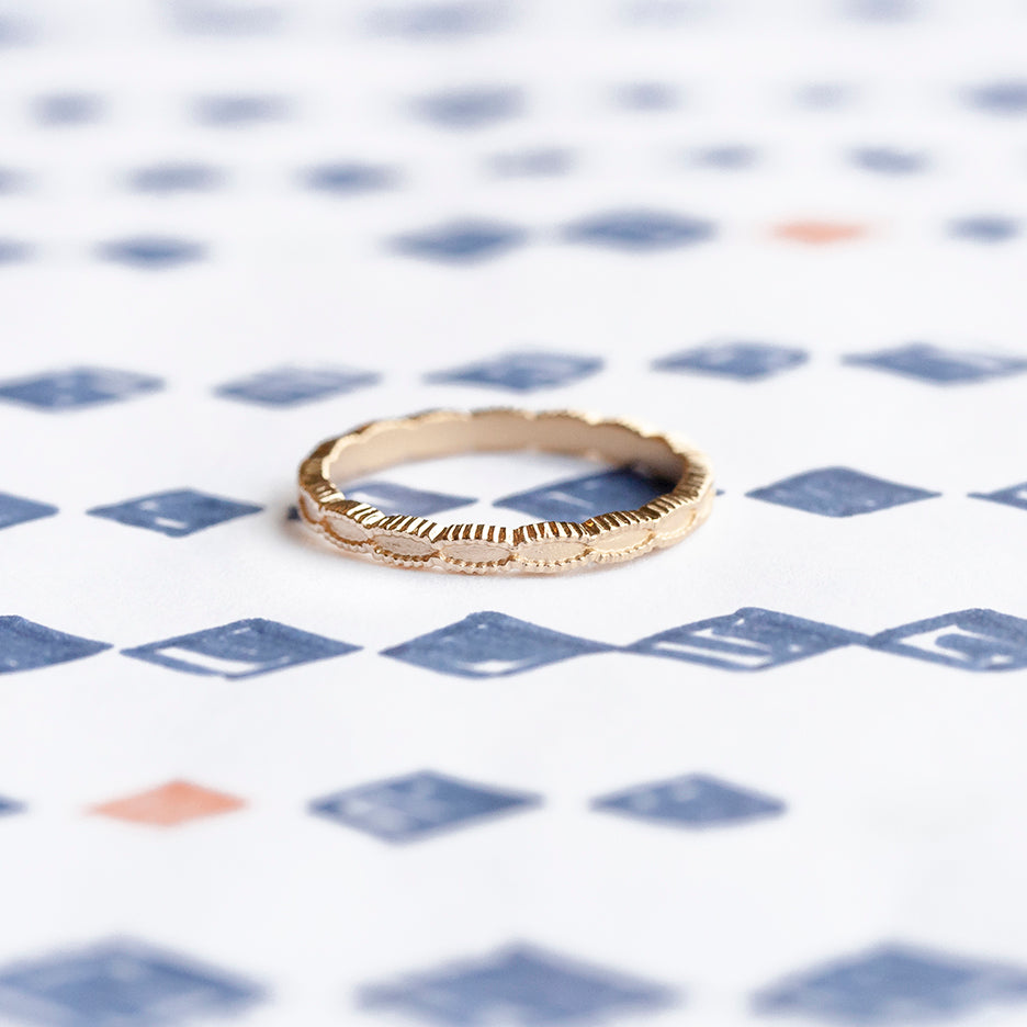 Handmade simple plain thin wedding band with scalloped ribbing in 18K yellow gold by Designer Megan Thorne on colored background