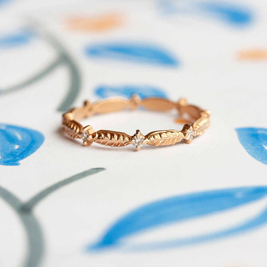 Handmade wedding or stacking band with diamonds and botanical Evergreen details in 18K rose gold by Designer Megan Thorne on colored background