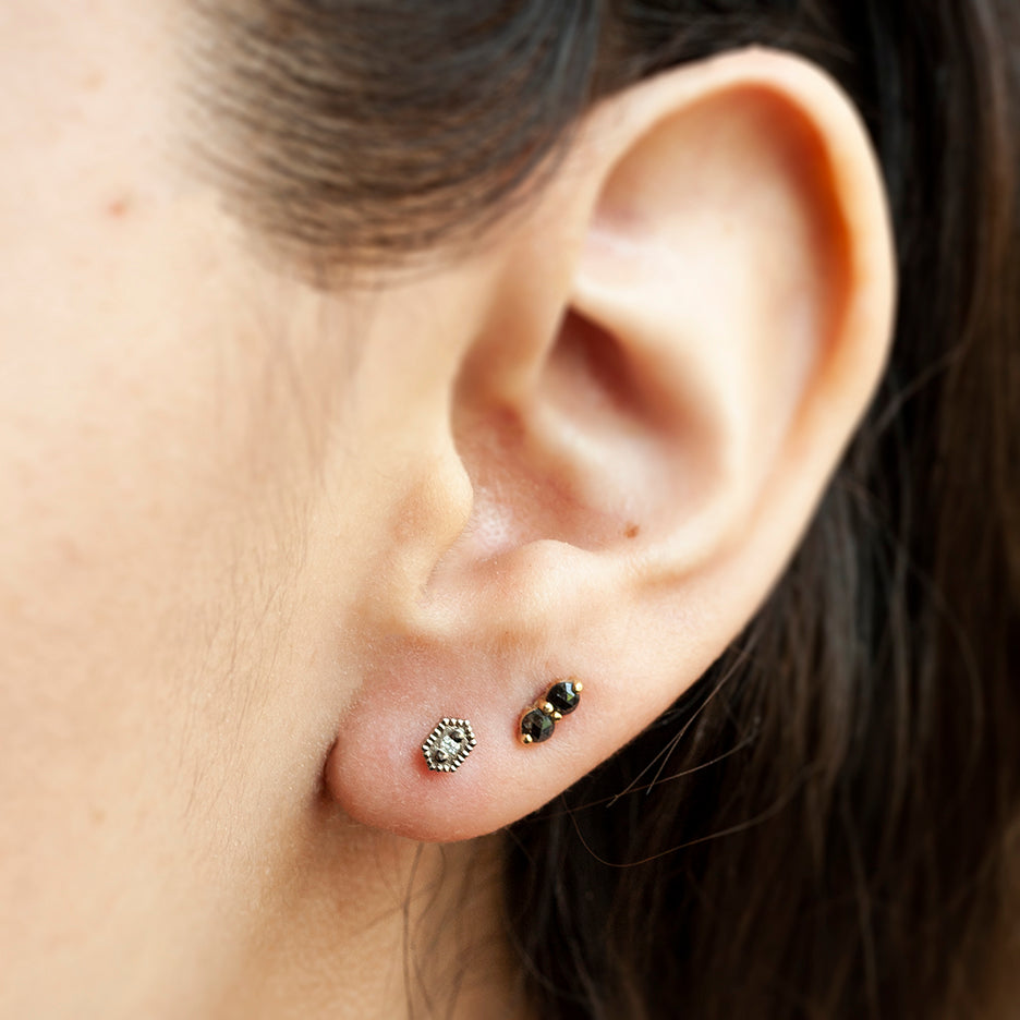 Handmade hexagon shaped stud earrings with ribbing, beading and diamonds in 18K white gold by Designer Megan Thorne pictured with bits and bobs black diamond studs on ear