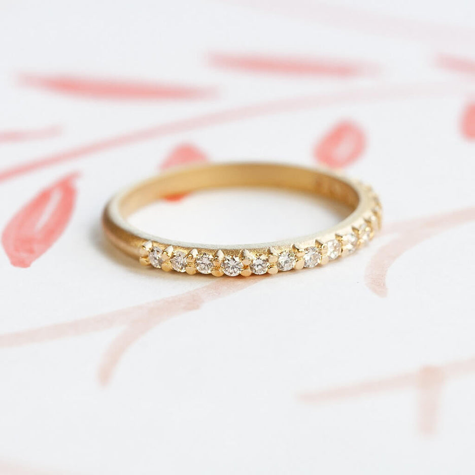 Handmade pave wedding or stacking band with diamonds and beading in 18K yellow gold by Designer Megan Thorne on colored background