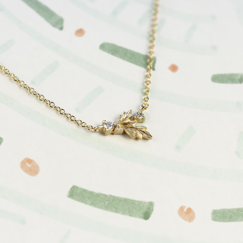 Handmade fine necklace with hand carved floral Wood Nymph details and diamond accents in 18K yellow gold by Designer Megan Thorne on colored background